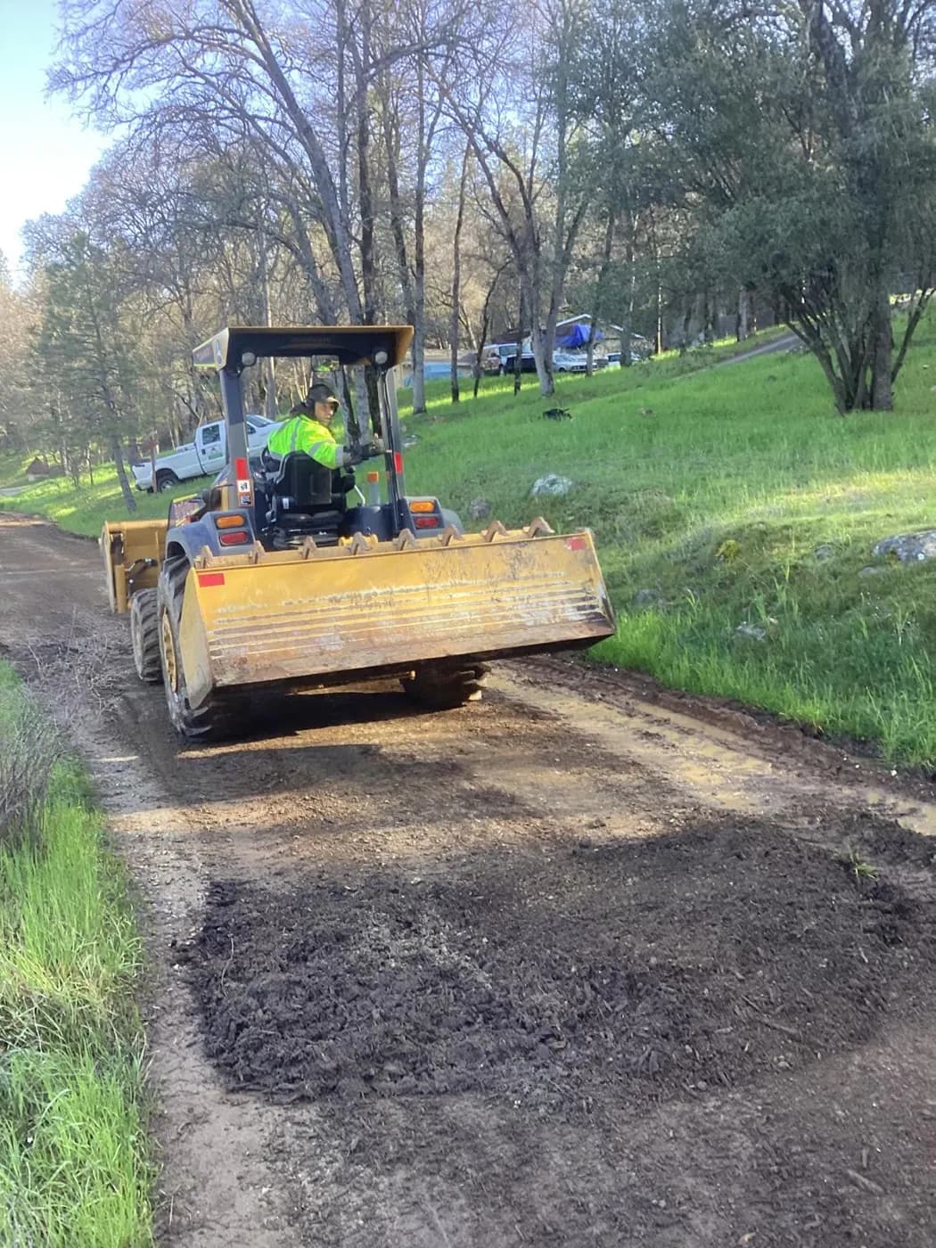 Ride-on roller compacting a resurfaced gravel driveway between grass verges