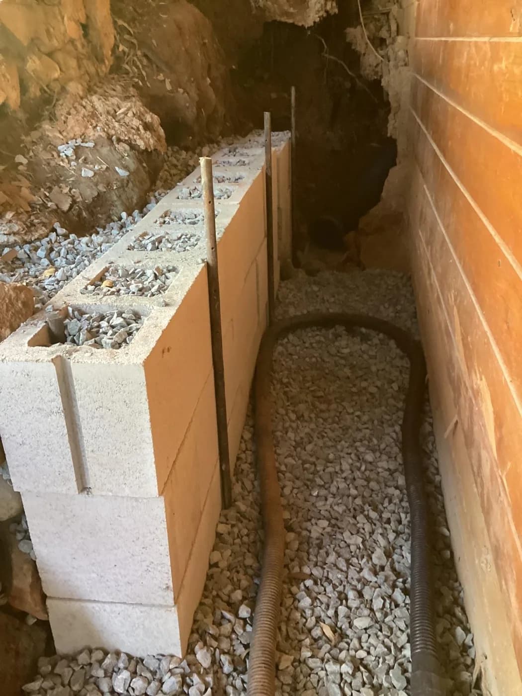 Drain rock and block backfill against a foundation wall in a hand-dug trench