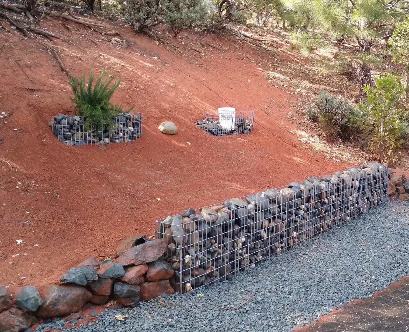 Gabion retaining wall of wire-caged rock along a gravel drive with boulder edging