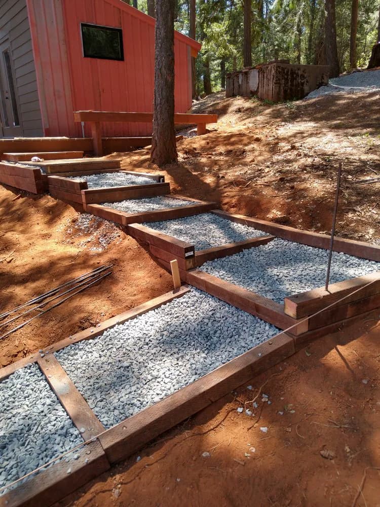 Timber-framed steps backfilled with crushed rock, cut into a slope beside an outbuilding