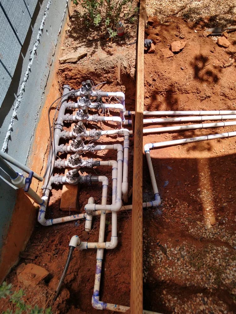 Six-valve irrigation manifold plumbed in an open trench along a foundation