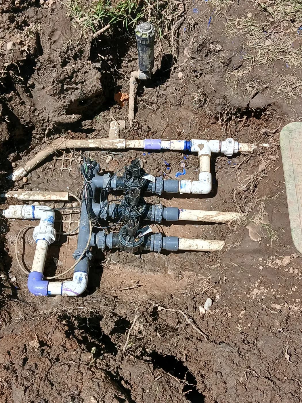 Sprinkler valve manifold dug out for repair with a rotor head reset alongside it