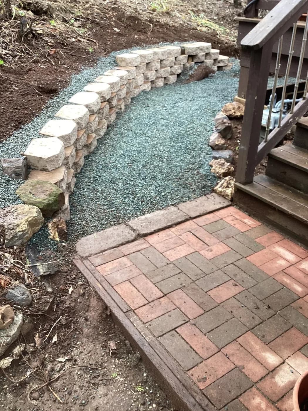 Stone retaining wall meeting a brick patio landing at the foot of a gravel path
